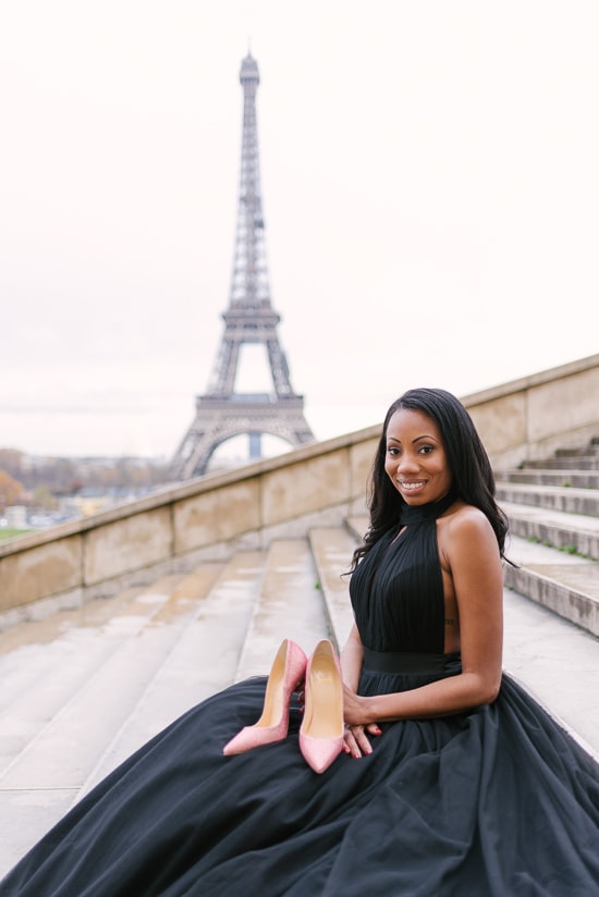 Beautiful black girl holding pink Louboutin high heels shoes in front of the Eiffel Tower in Paris