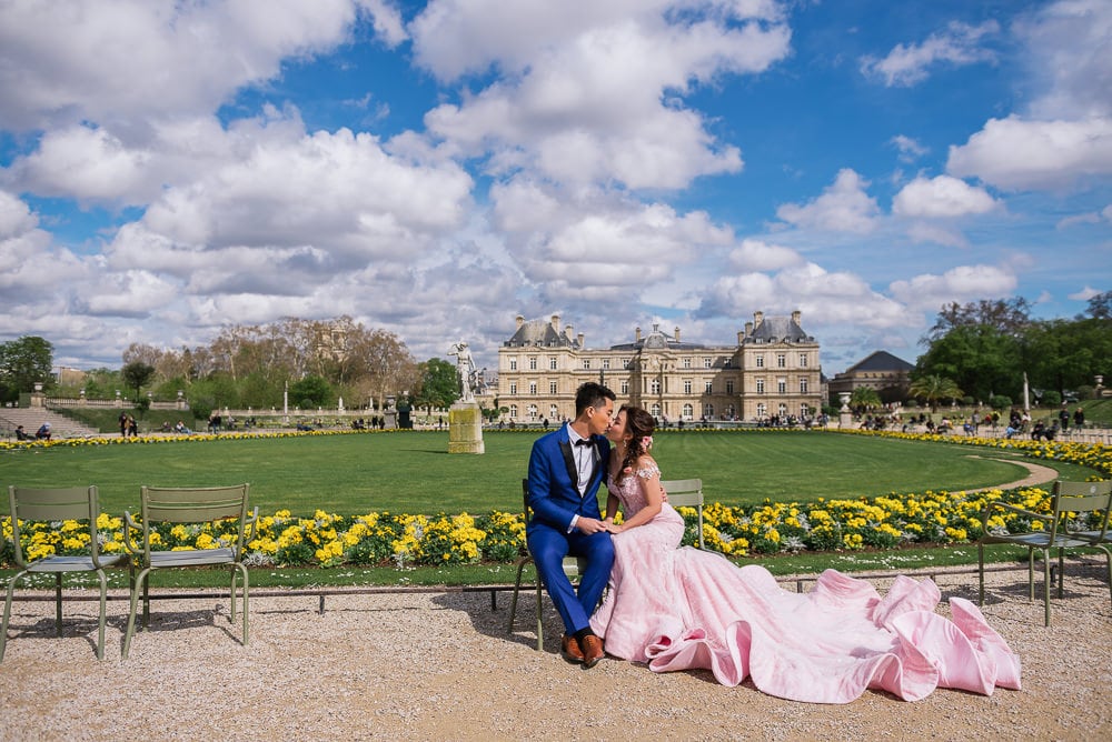 Blue sky, white clouds, Luxembourg gardens casstle and pre wedding couple with rich pink dress kissing