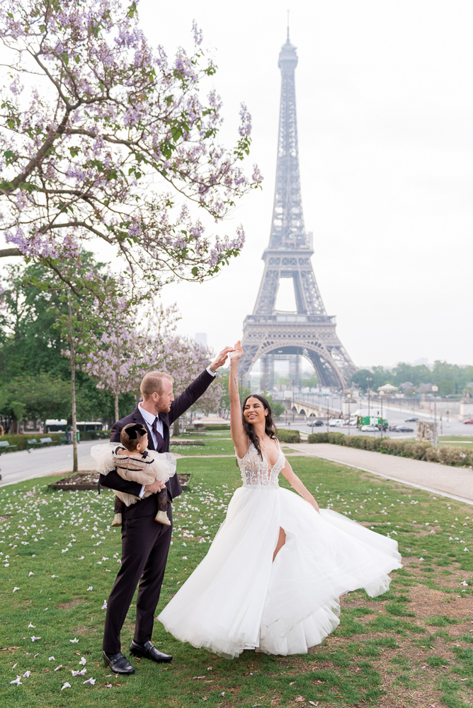 Bride dancing in front of the Eiffel Tower, holding hand of groom with baby in other hand