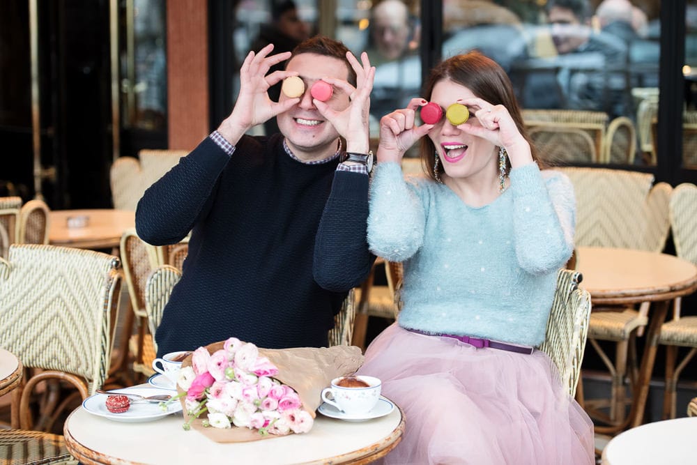 Couple having fun with colorful macarons in a parisian café