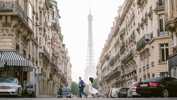 Couple running across the street during their engagement photo shoot in Paris at the Eiffel Tower