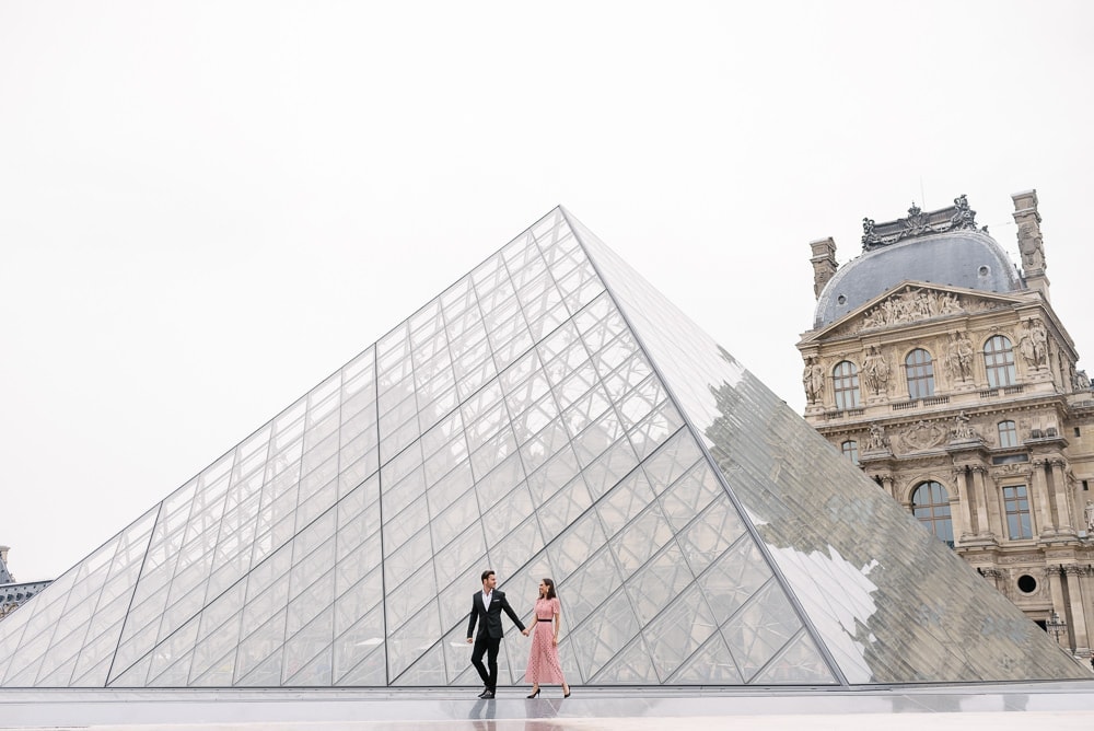 Couple walking on water in front of the big pyramid of the Louvre Museum