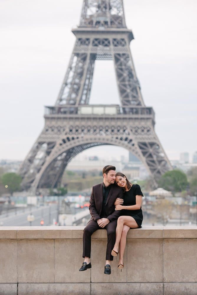 fun couple photoshoot ideas - sitting on a wall in front of the Eiffel Tower