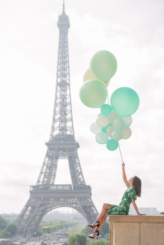 Indonesian girl holding green balloons is posing in front of the Eiffel Tower during a mid day photo shoot with The Paris Photographer