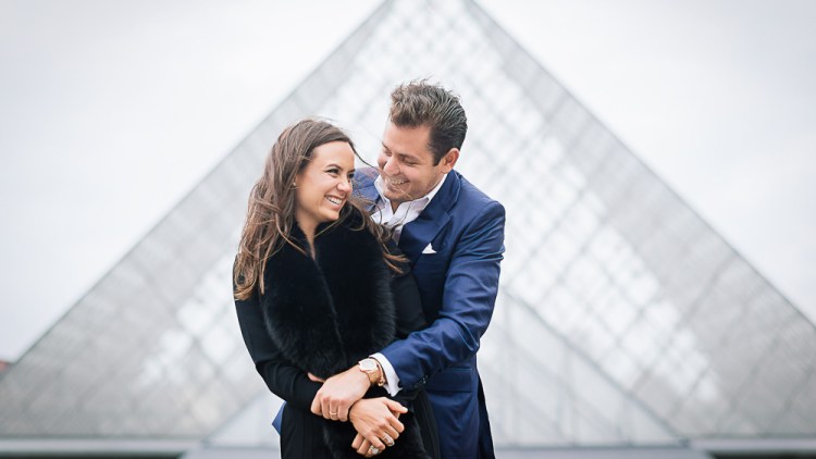 Married couple posing in front of the Louvre Pyramid for their honeymoon photos