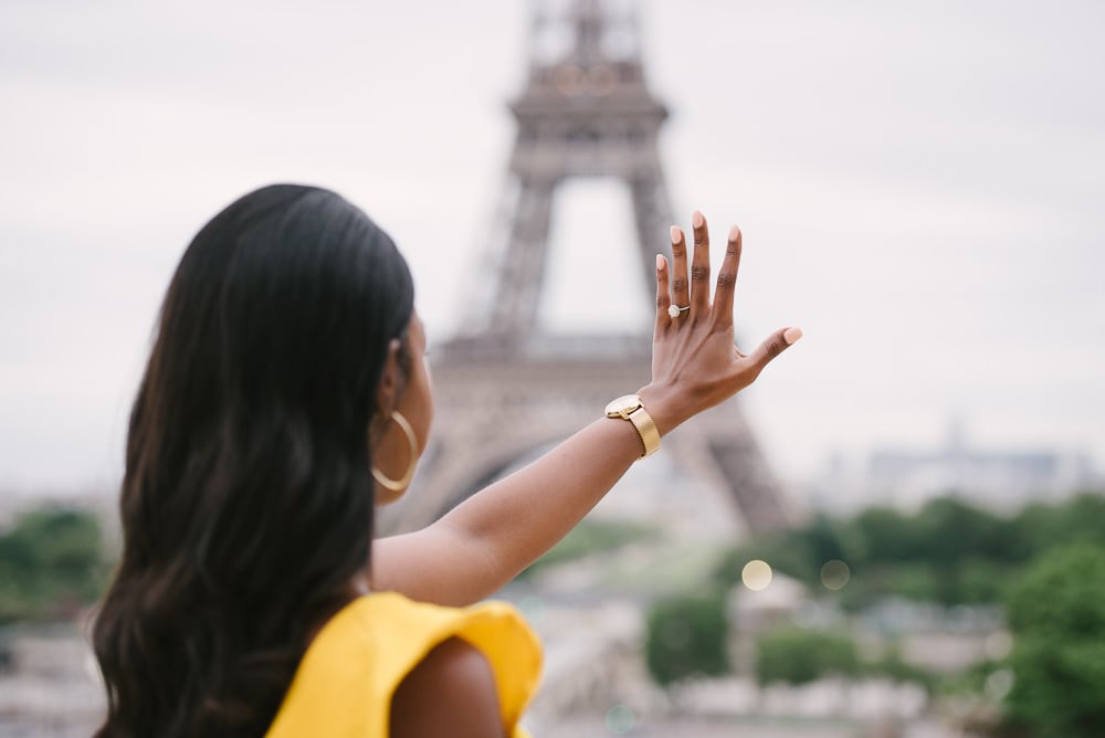 Newly engaged girl looking at diamond ring on her hand at the Eiffel Tower in Paris