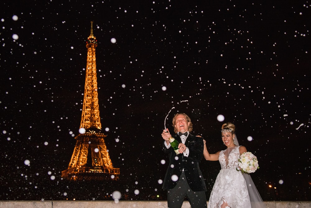 Paris elopement photographer - Bride and groom celebrate with champagne pop in front of the Eiffel Tower by night