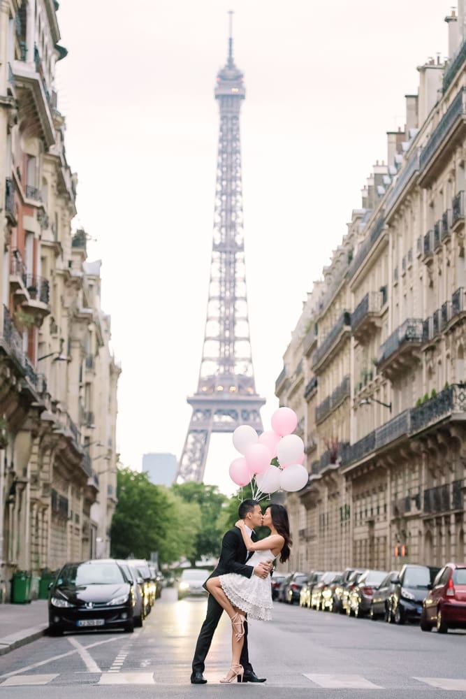 paris engagement photos kissing in the middle of the street with haussmanian buildings on both sides and the eiffel tower in the background 2