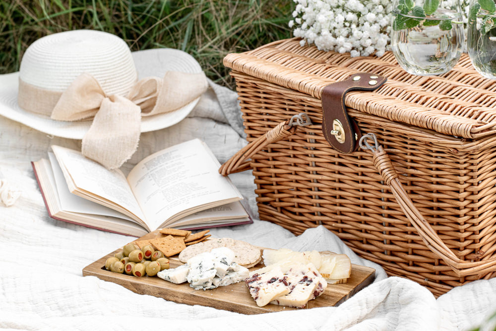 Picnic set up with basket cheese a book and a hat
