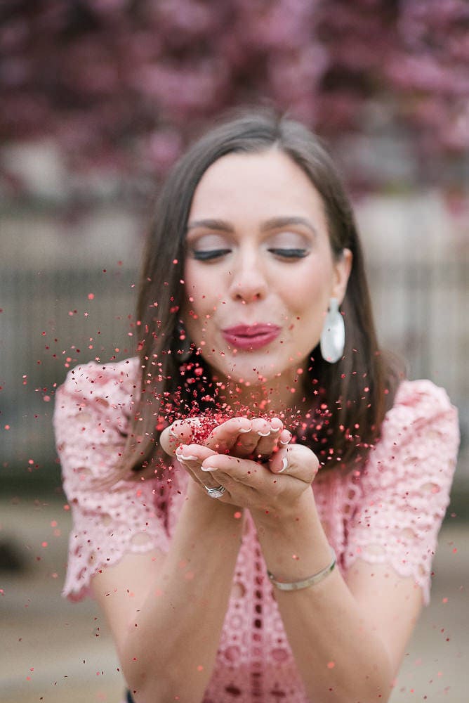 Pretty girl blowing in pink confetti in Paris