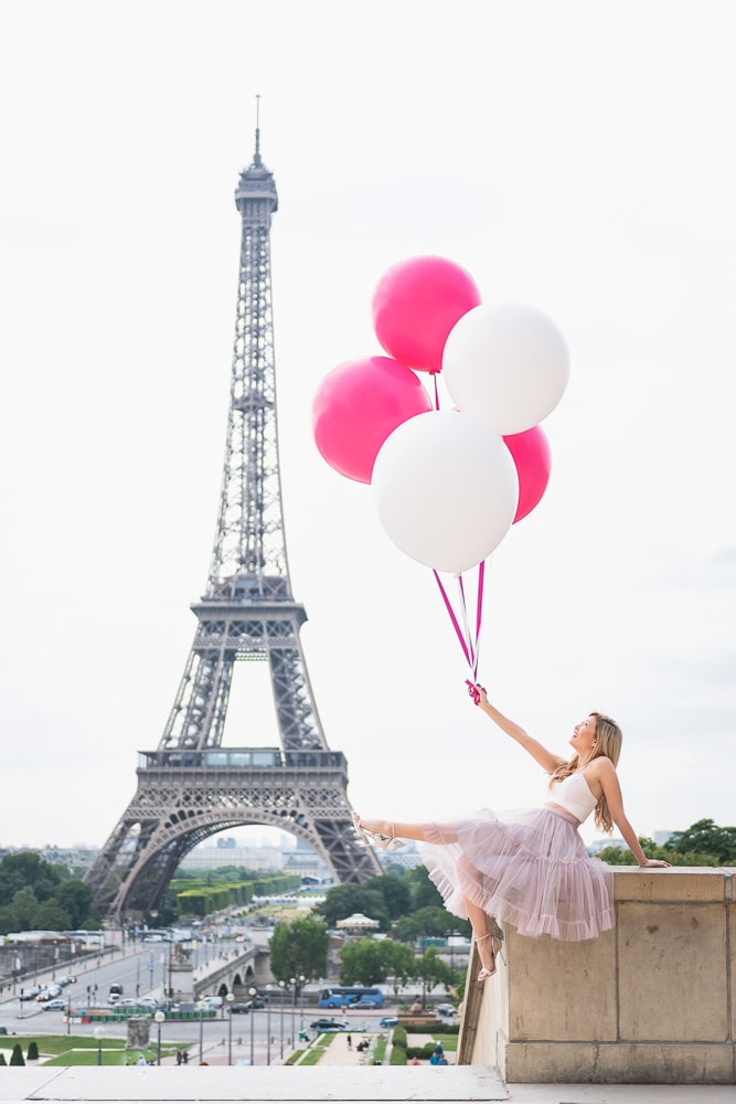 Pretty girl wearing pink tutu dress holding pink balloons at the Eiffel Tower